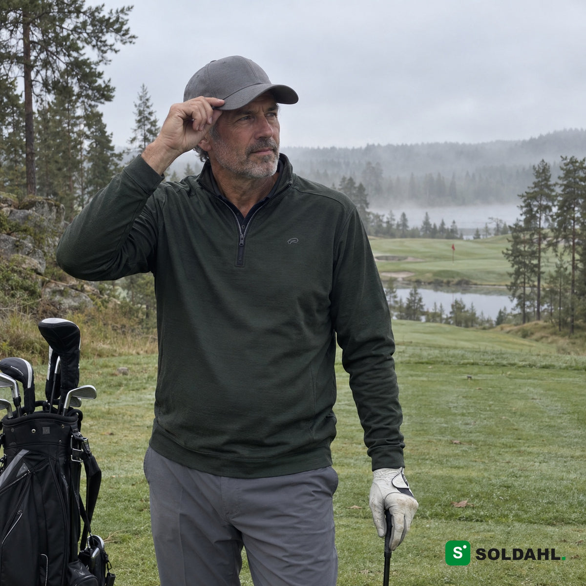 Golfare i grön tröja som justerar en grå keps på en dimmig golfbana