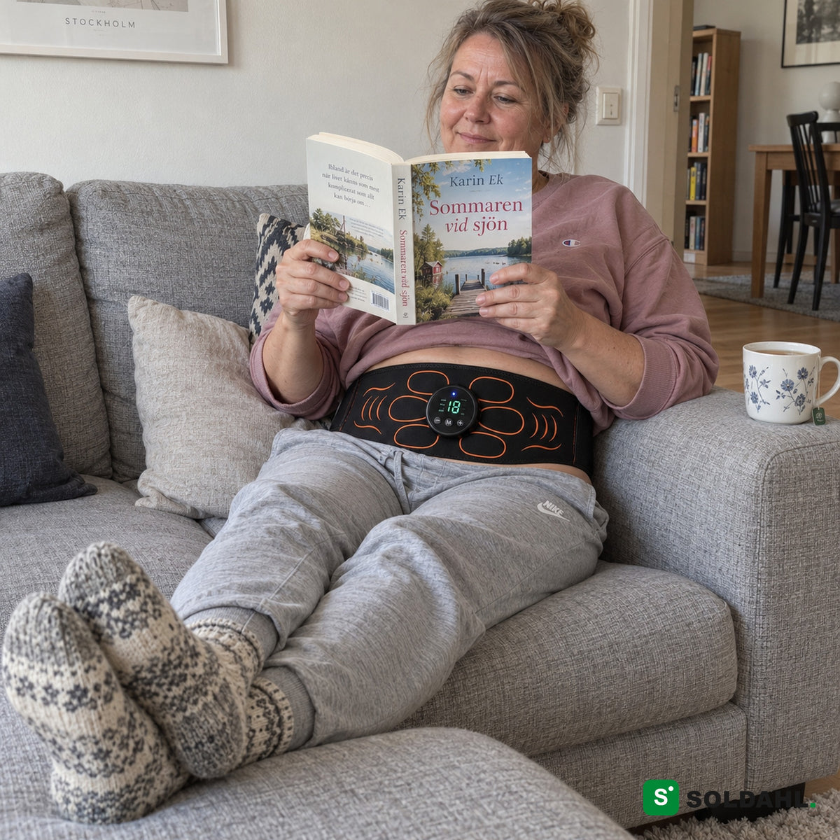 Kvinna läser en bok i soffan med magbältet runt magen