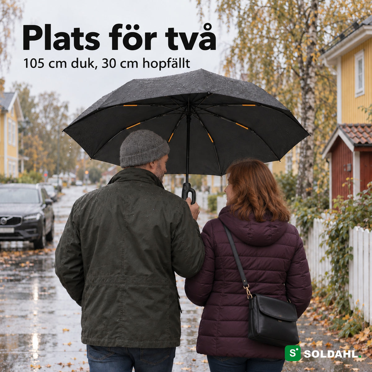 Två vuxna går tillsammans under ett Stormparaply på en regnig villagata